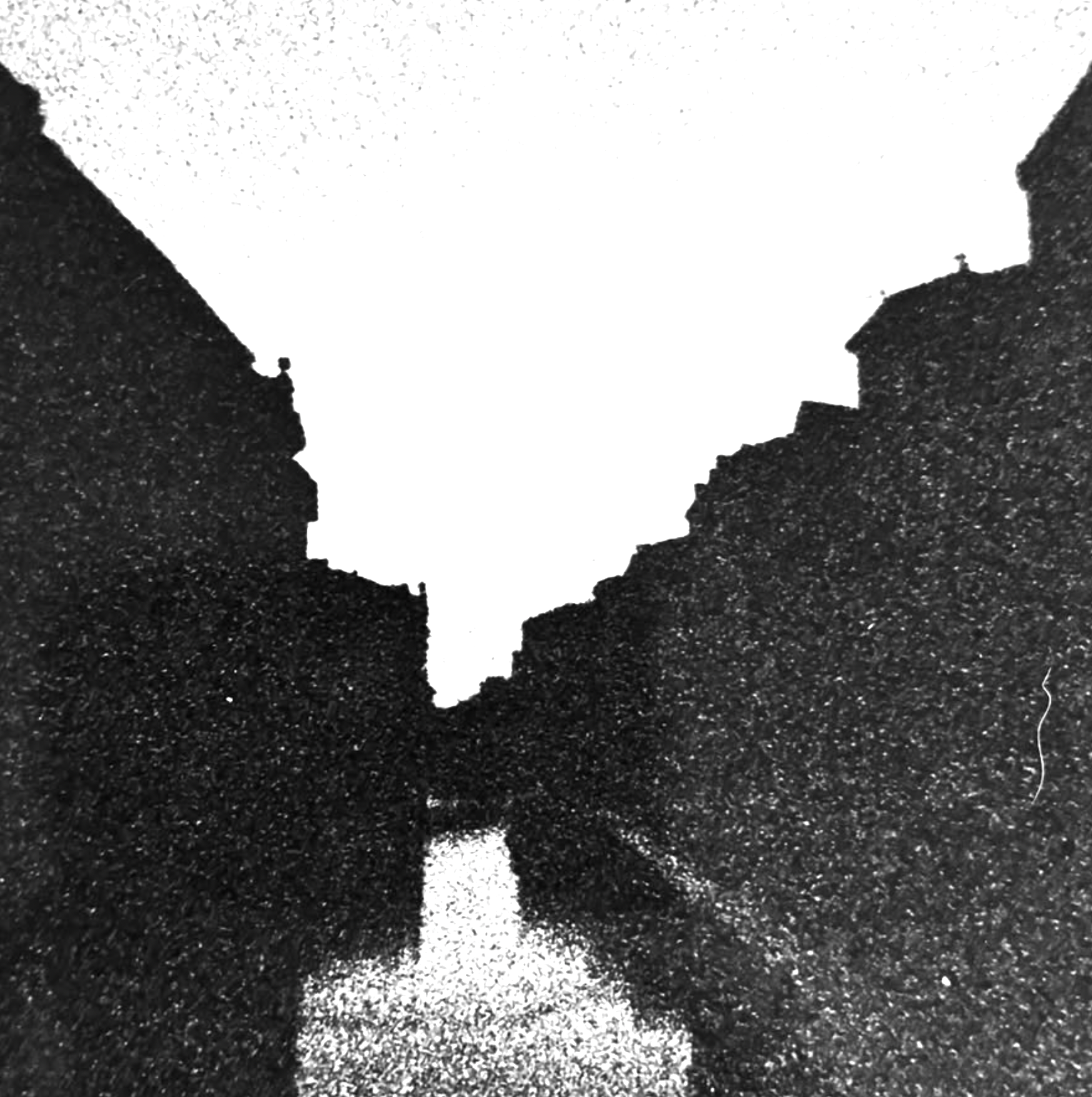 A person looking up between dark city buildings toward the bright sky
